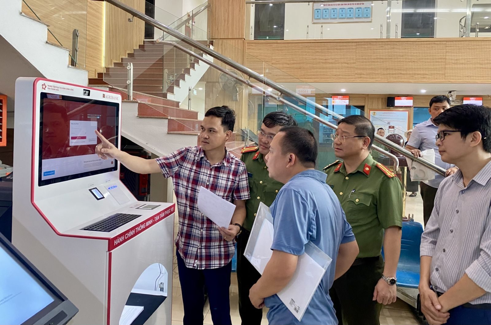Người dân thao tác trên kiosk thông minh tại Trung tâm Phục vụ hành chính công, có cán bộ công an đứng cạnh hướng dẫn